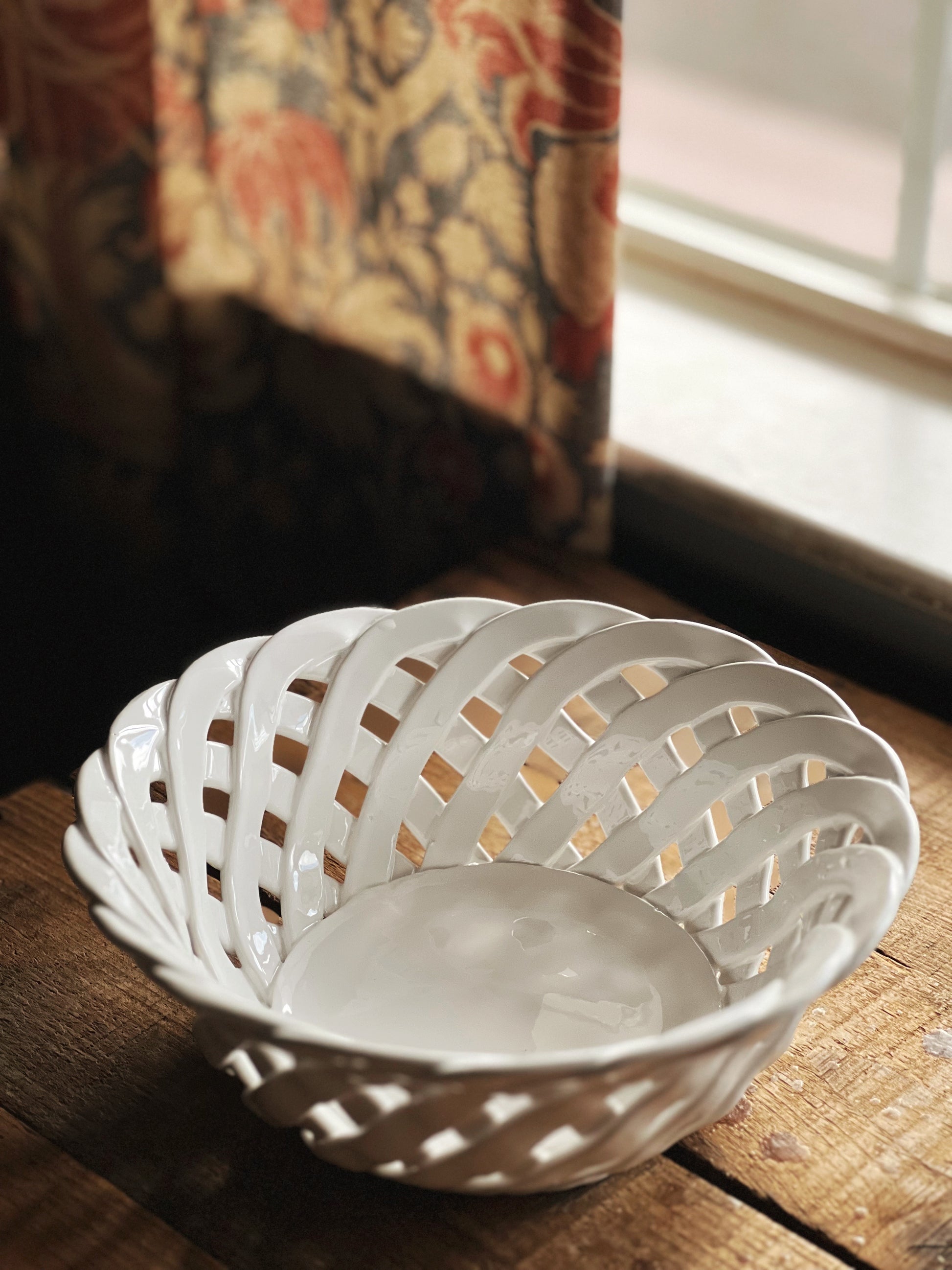 Decorative ceramic dish with floral patterns on a checkered cloth, with a blurred background of a scenic painting.