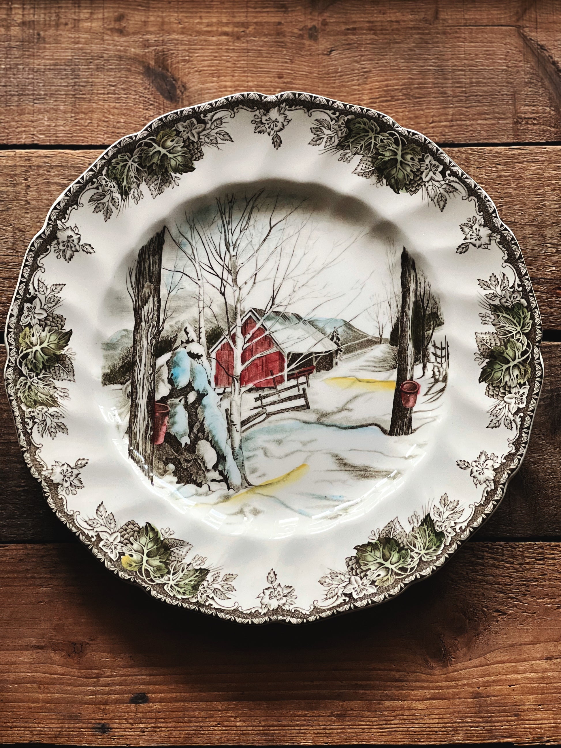 Decorative plate with a winter scene of a red cabin on a wooden surface
