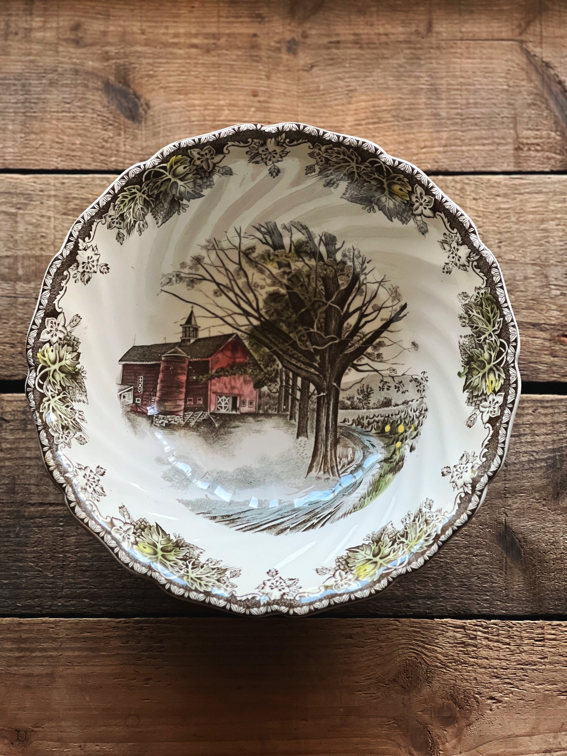 Decorative plate with a scenic design of a barn and tree on a wooden surface
