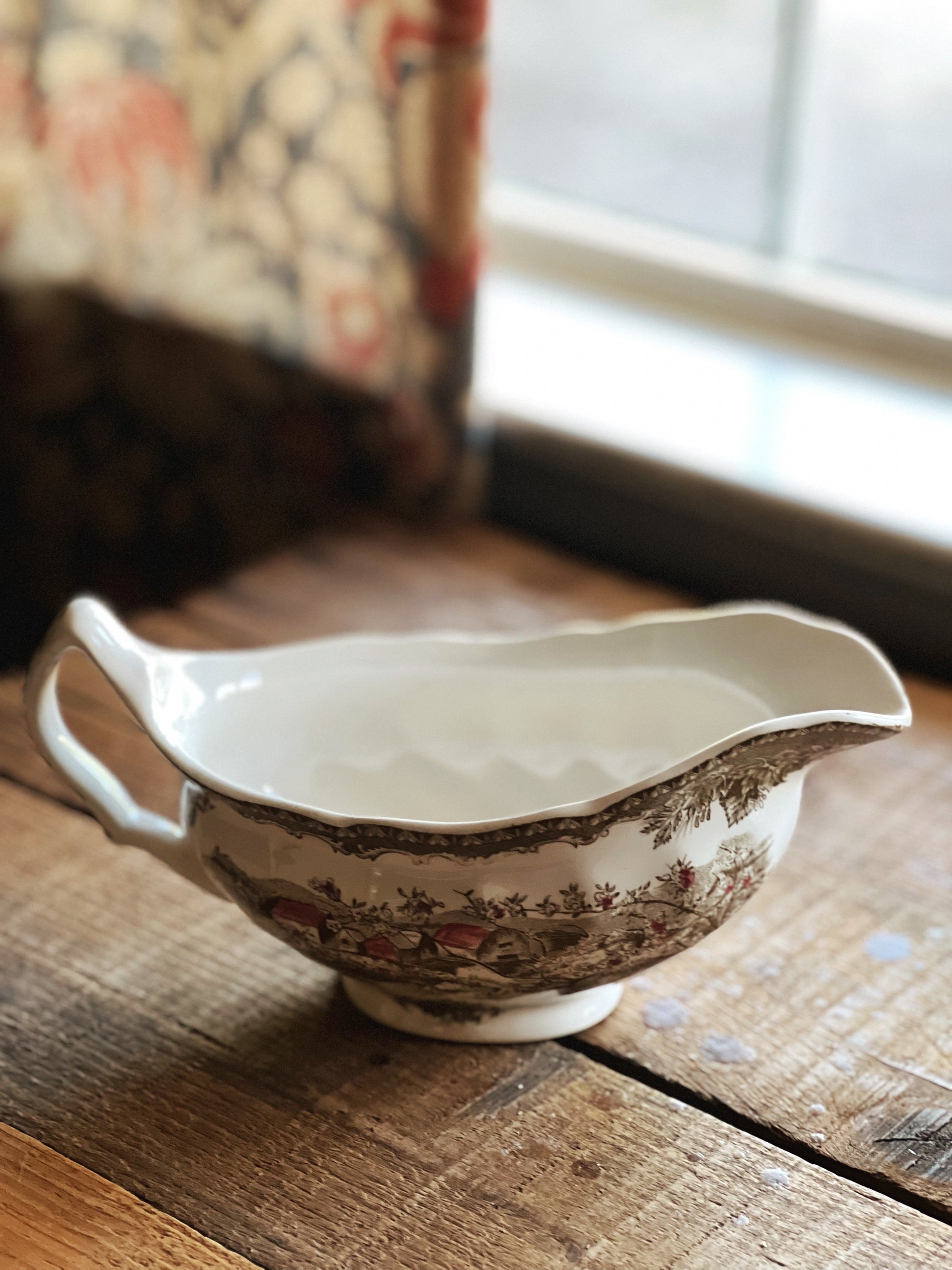 Vintage-style ceramic gravy boat on a wooden surface with a blurred background