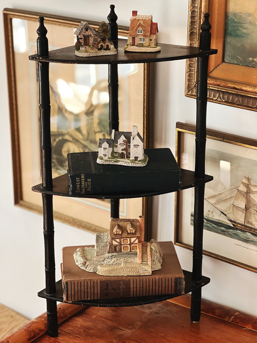 Black corner shelf with decorative items against a wall with framed pictures