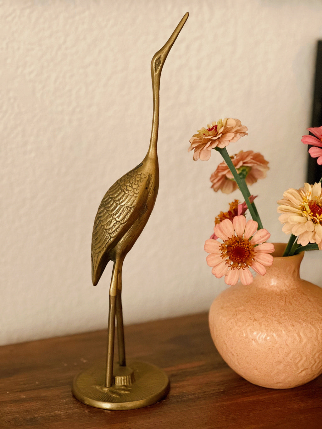 Bronze crane sculpture next to a vase with flowers on a wooden surface