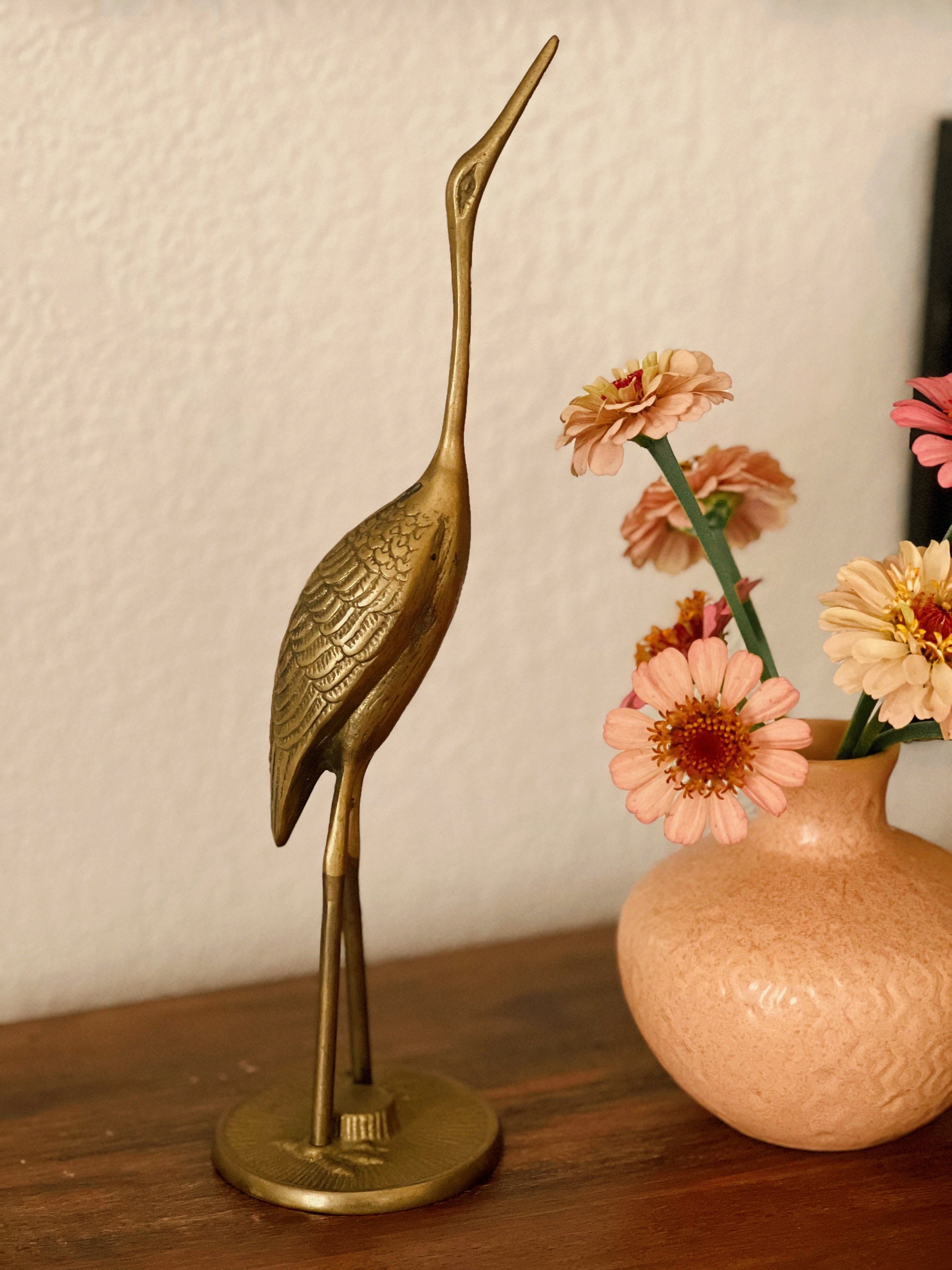Bronze crane sculpture next to a vase with flowers on a wooden surface
