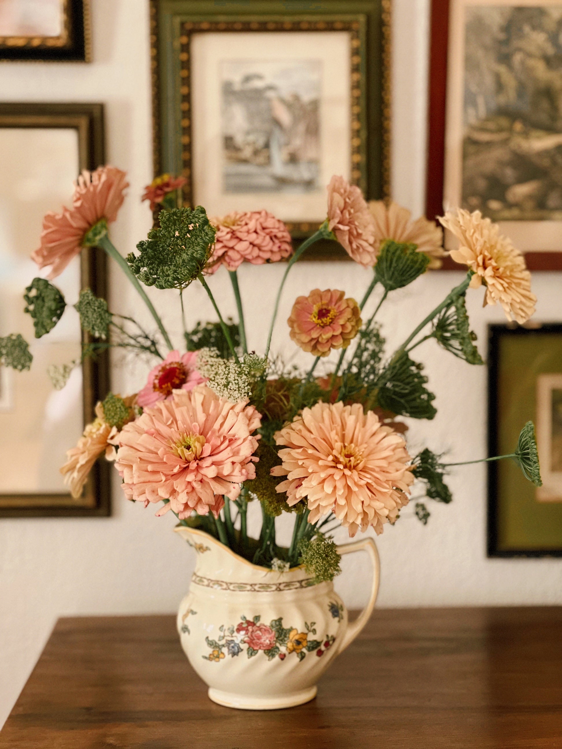 Vintage-style pitcher with peach-colored flowers against a wall with framed pictures