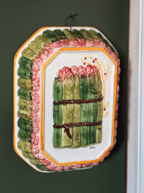 Decorative plate with a design of green asparagus and pink flowers on a dark background