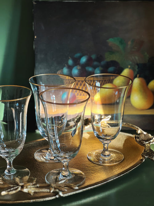 Set of clear glasses on a silver tray with a still life painting in the background