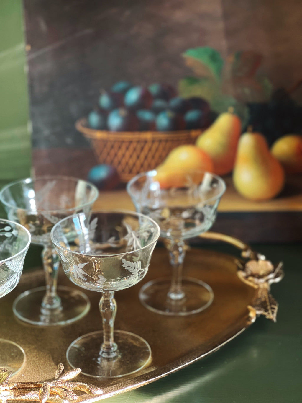 Clear glass goblets on a decorative tray with a blurred background of fruits and a basket.