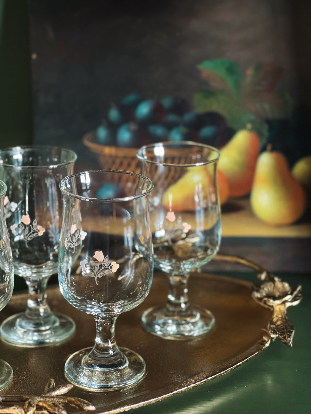 Set of decorative glass goblets on a wooden tray with fruit in the background