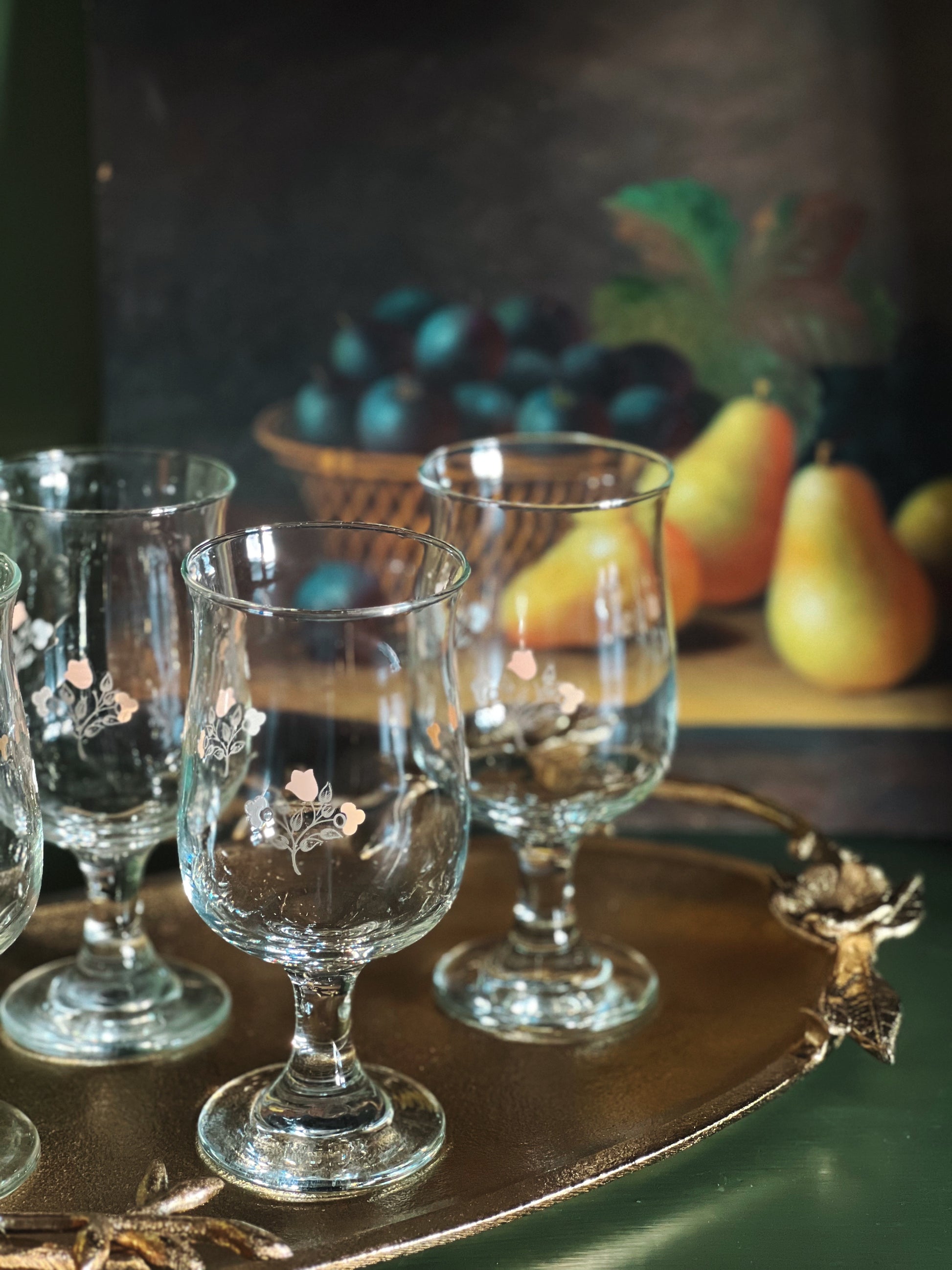 Set of decorative glass goblets on a wooden tray with fruit in the background