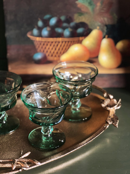 Green glass compotes on a decorative tray with a fruit basket in the background