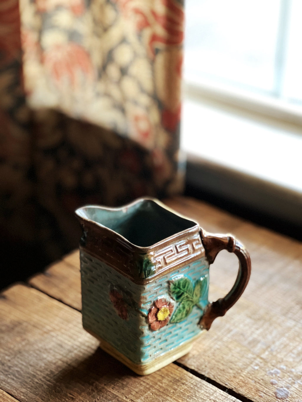 Decorative ceramic pitcher on a wooden surface with a window in the background