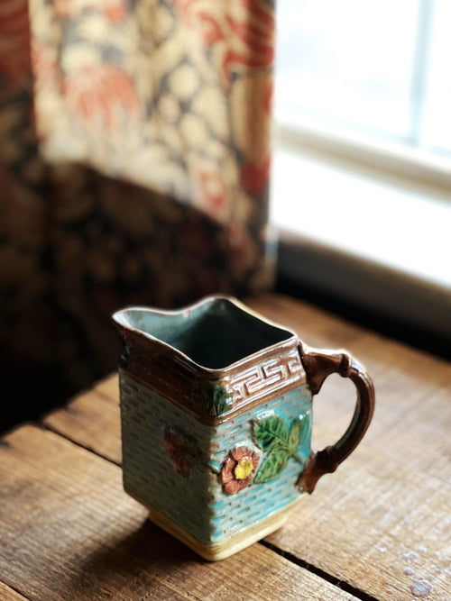 Decorative ceramic pitcher on a wooden surface with a window in the background