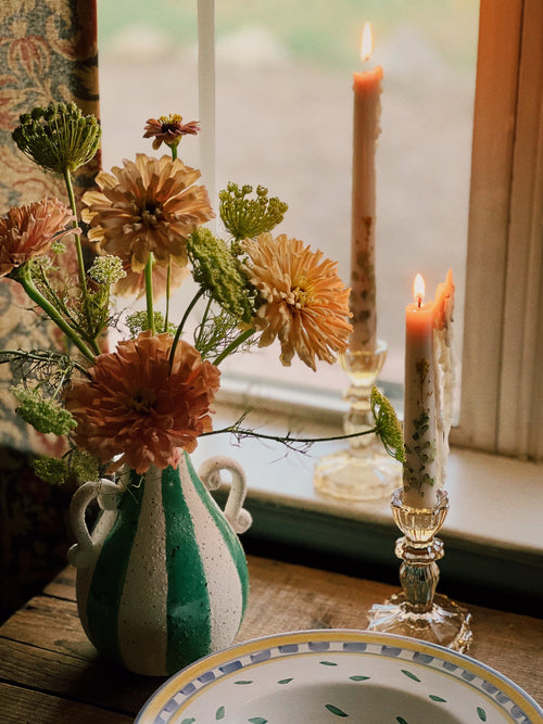 Vase with flowers and candles on a table near a window
