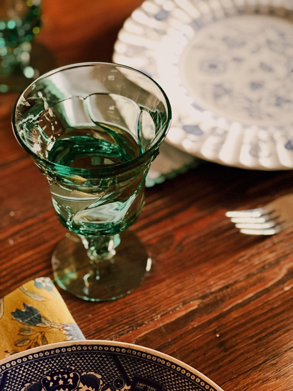 Green glass on a wooden table with decorative plates and cutlery in the background