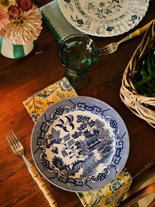 Blue and white patterned plate on a wooden table with floral decorations and cutlery.