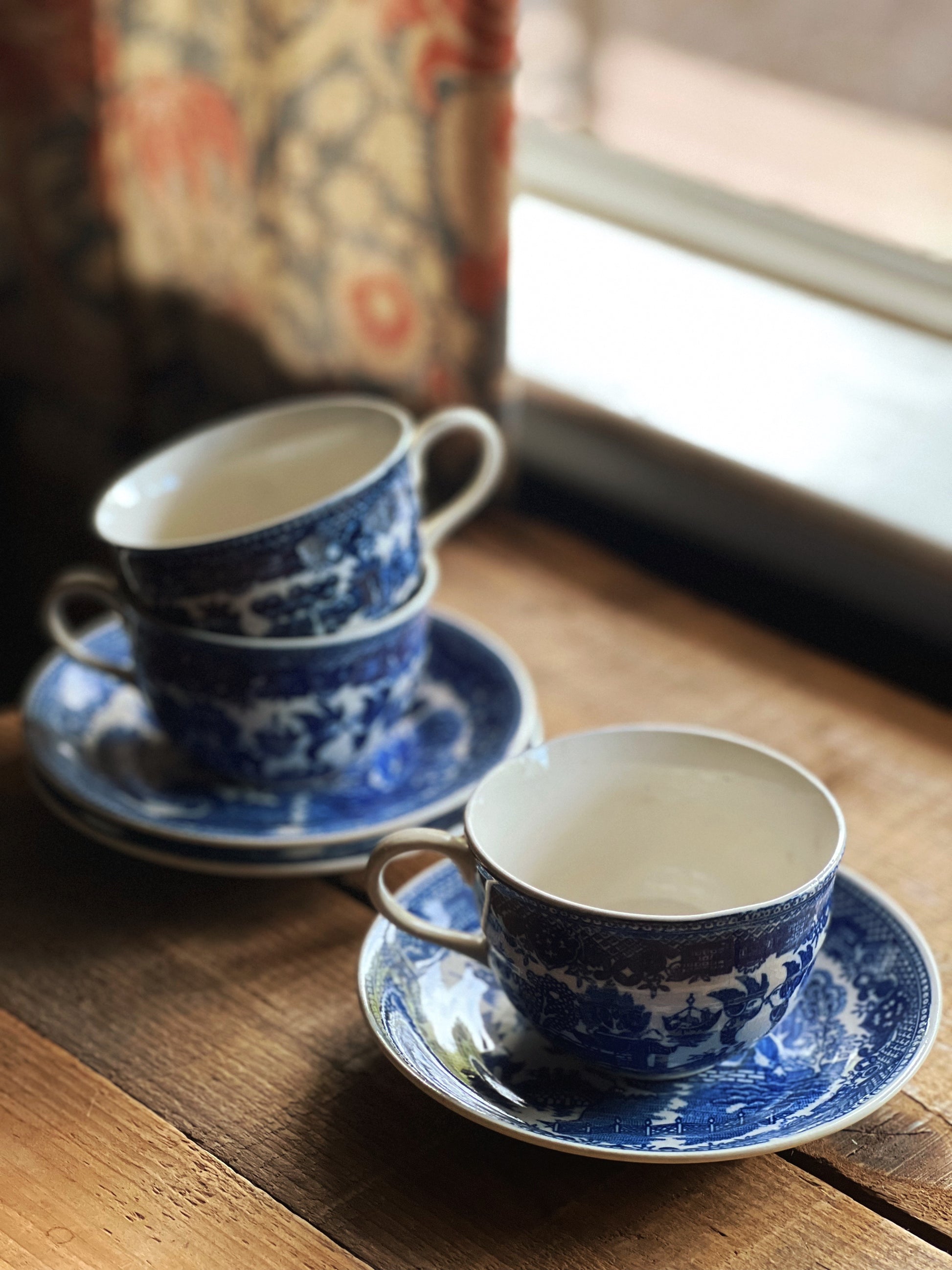 Two blue and white teacups and saucers on a wooden table with a window in the background.