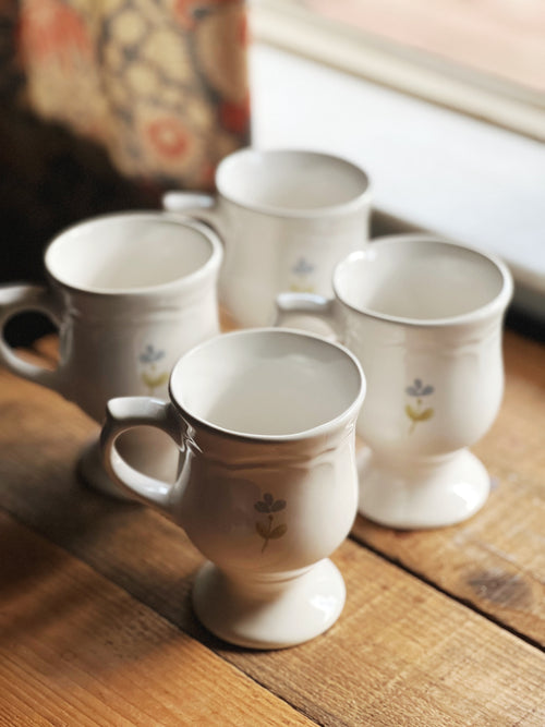 Set of white ceramic mugs with floral designs on a wooden surface