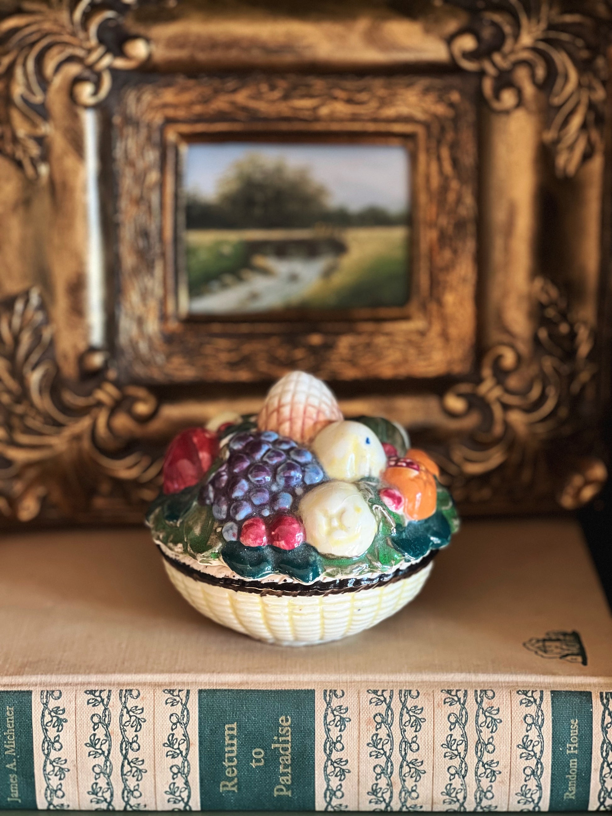 Decorative bowl with fruits and vegetables on a book with a gold frame in the background