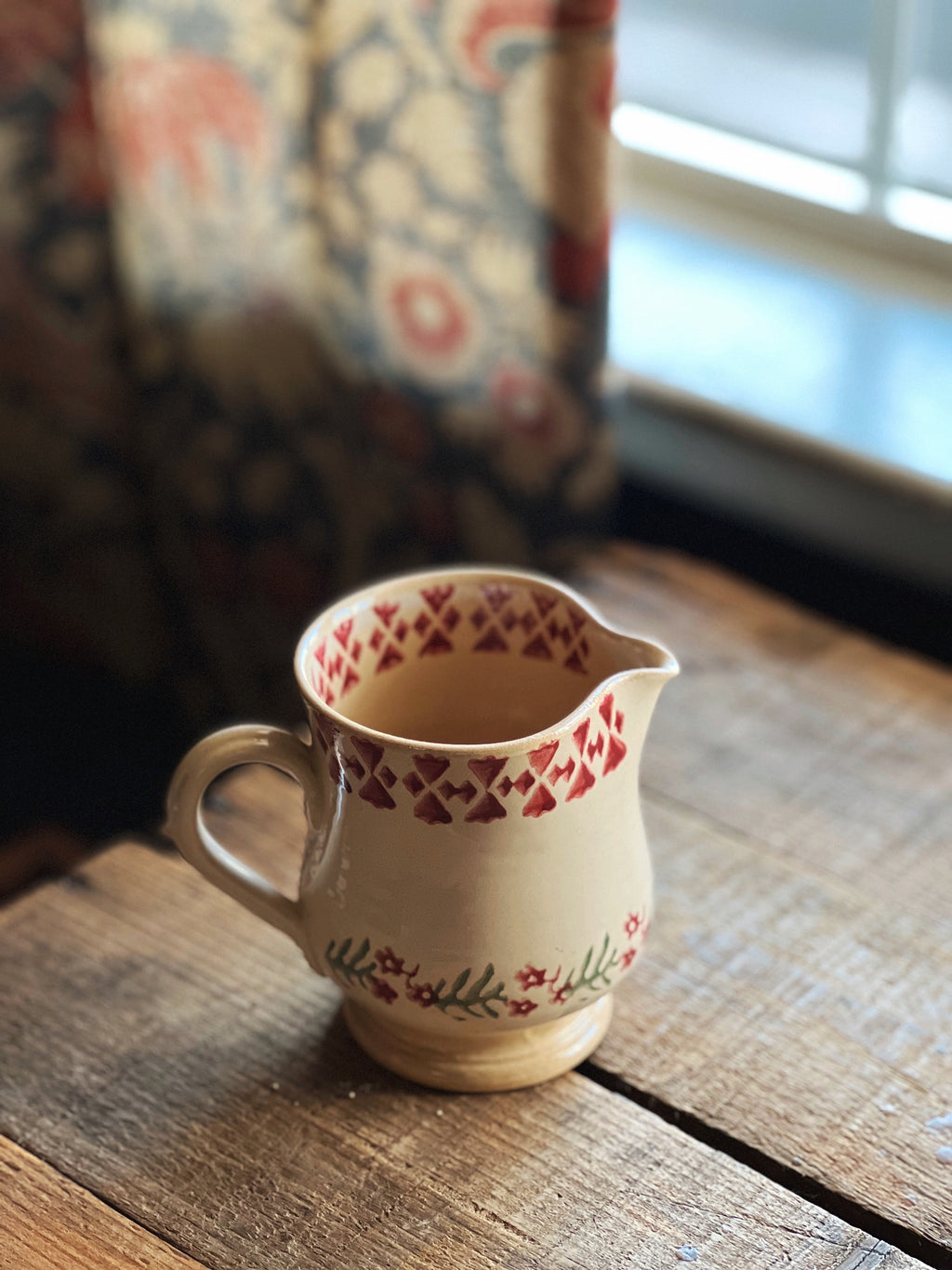 Small ceramic pitcher with floral patterns on a wooden surface