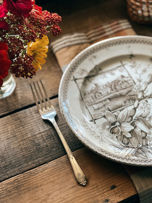Decorative plate with floral design on a wooden table with flowers and a fork.