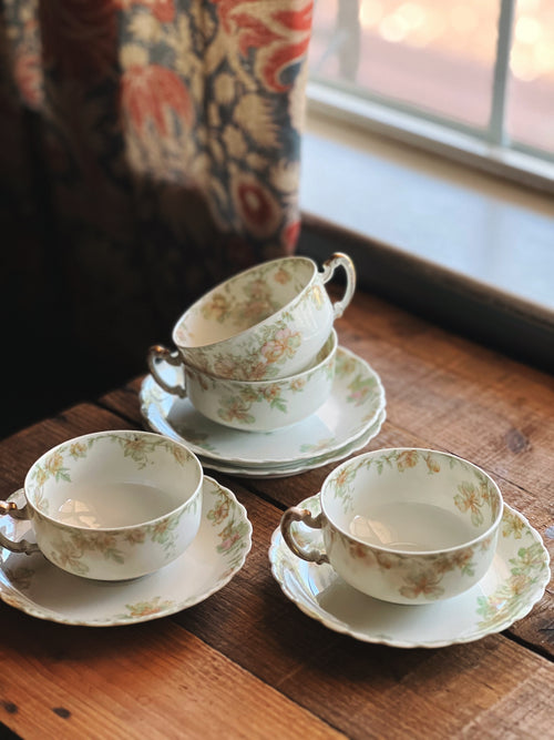 Set of floral teacups and saucers on a wooden surface with a window in the background.