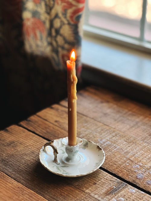 Candle in a decorative holder on a wooden surface with a window in the background