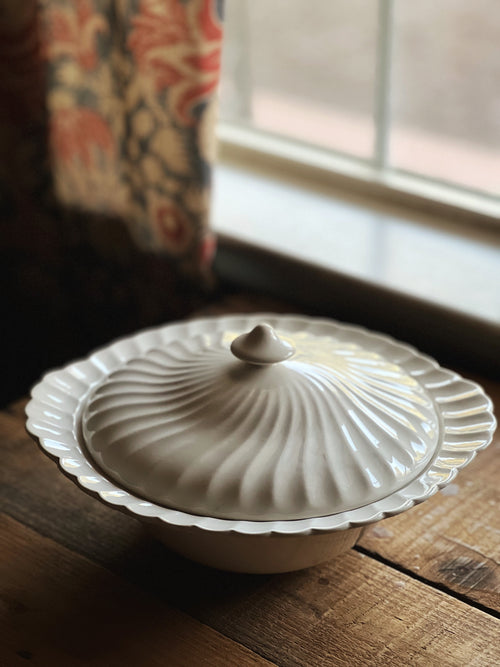 White ceramic dish with lid on a wooden surface near a window