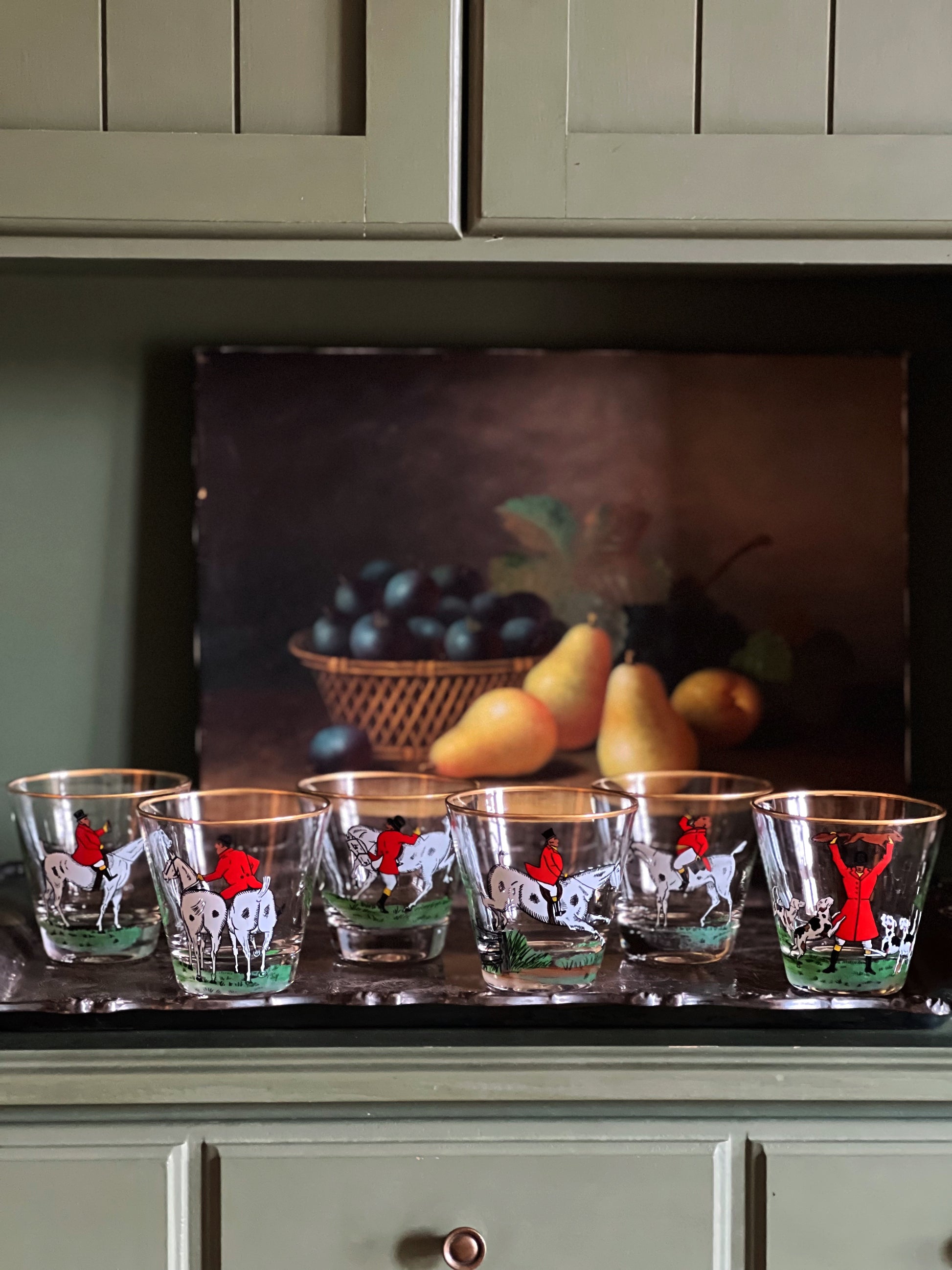 A vintage two-handle silver serving tray with a dark, heavy patina and a decorative element in the center, displayed in front of a wall with fruit illustration.