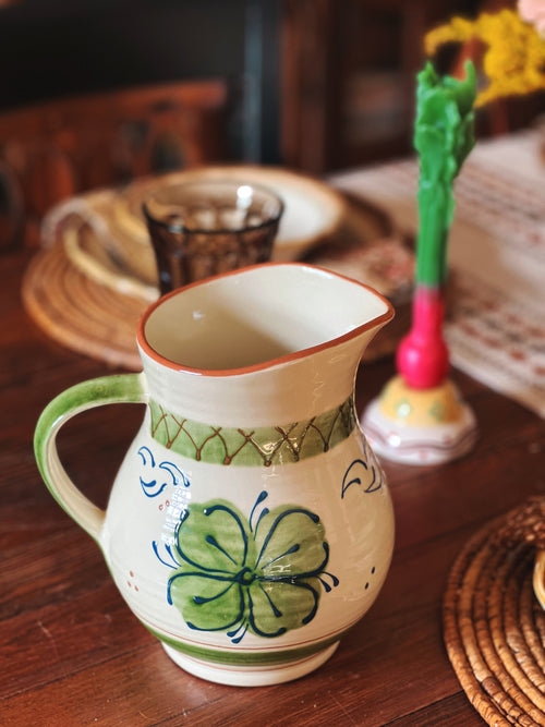 Ceramic pitcher with green floral design on a wooden table