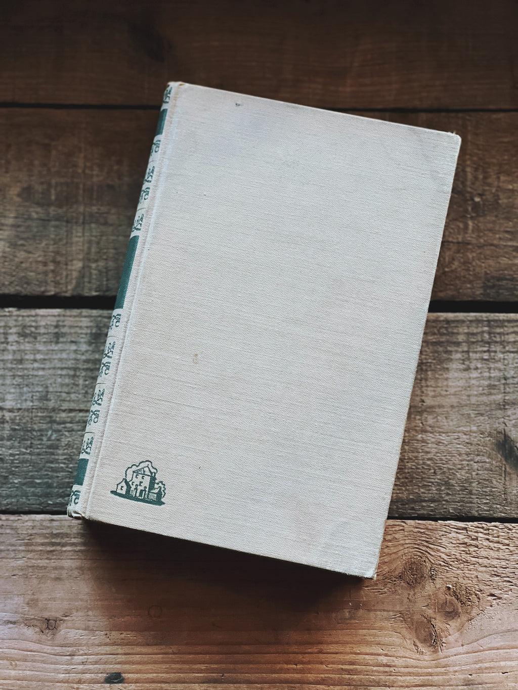 A vintage hardcover book with a beige cover and a small, decorative emblem in the center.