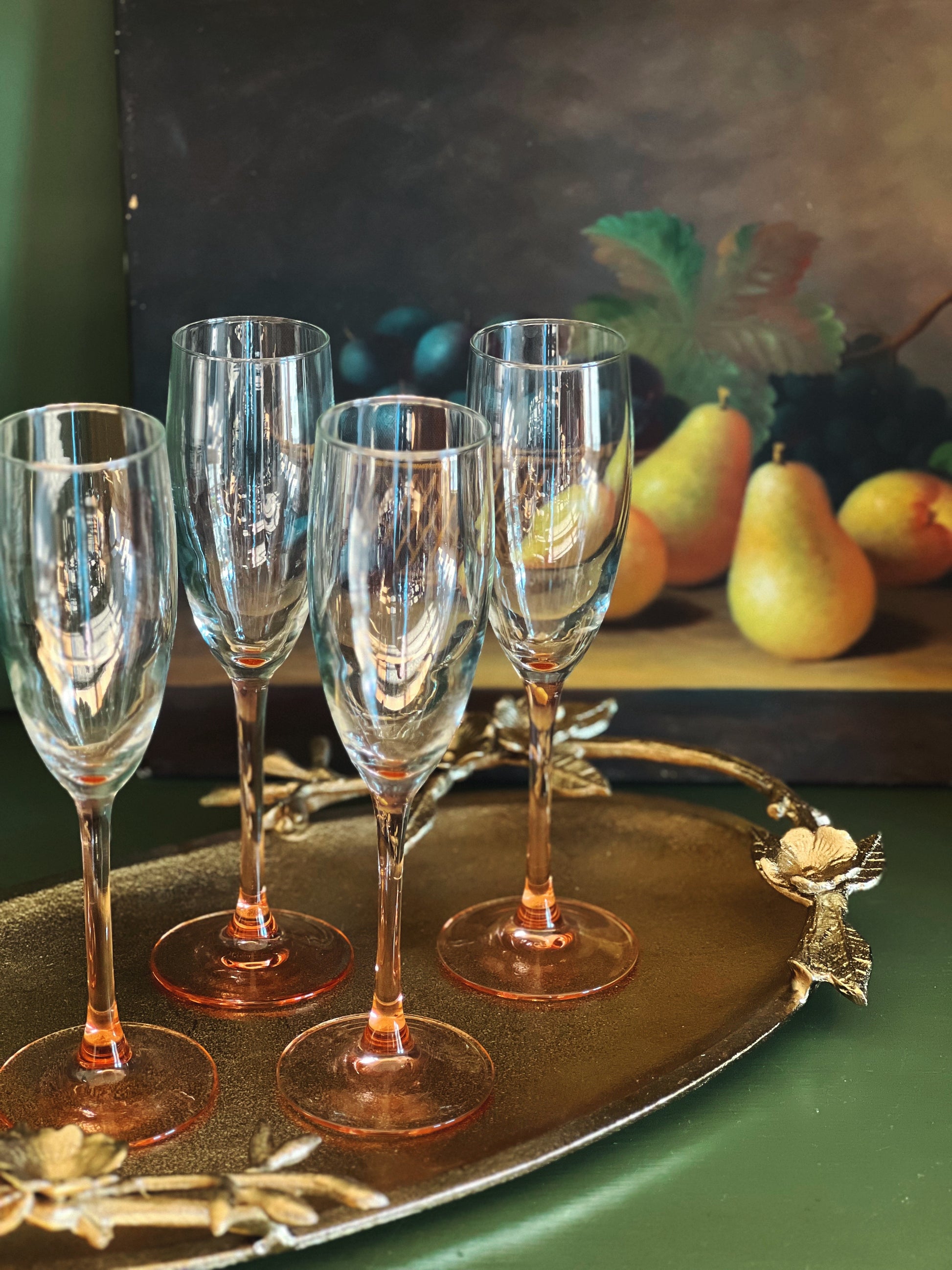 Set of four wine glasses on a decorative tray with fruit in the background