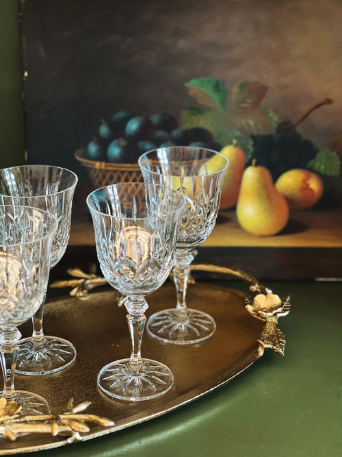 Set of crystal glasses on a decorative tray with a fruit still life painting in the background.