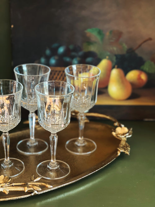 Set of crystal wine glasses on a decorative tray with fruit in the background
