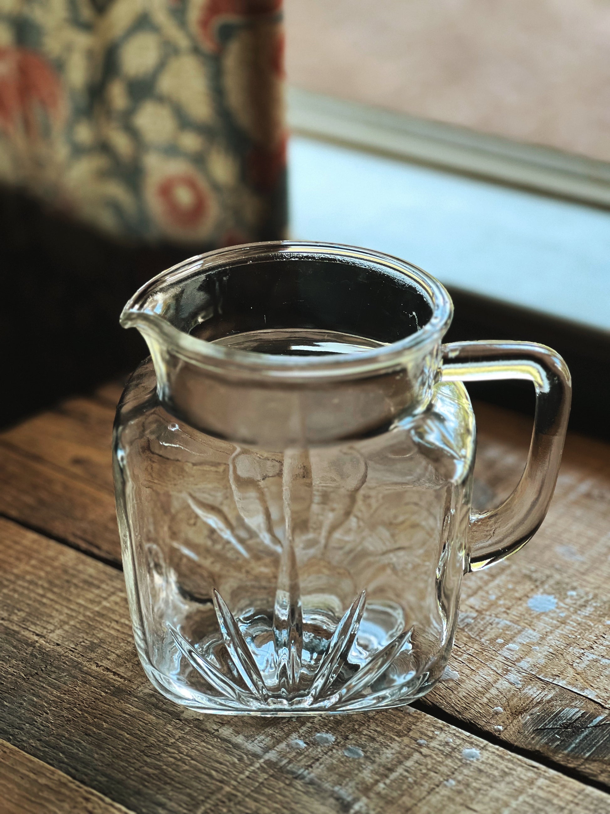 Clear glass pitcher with handle on a wooden surface