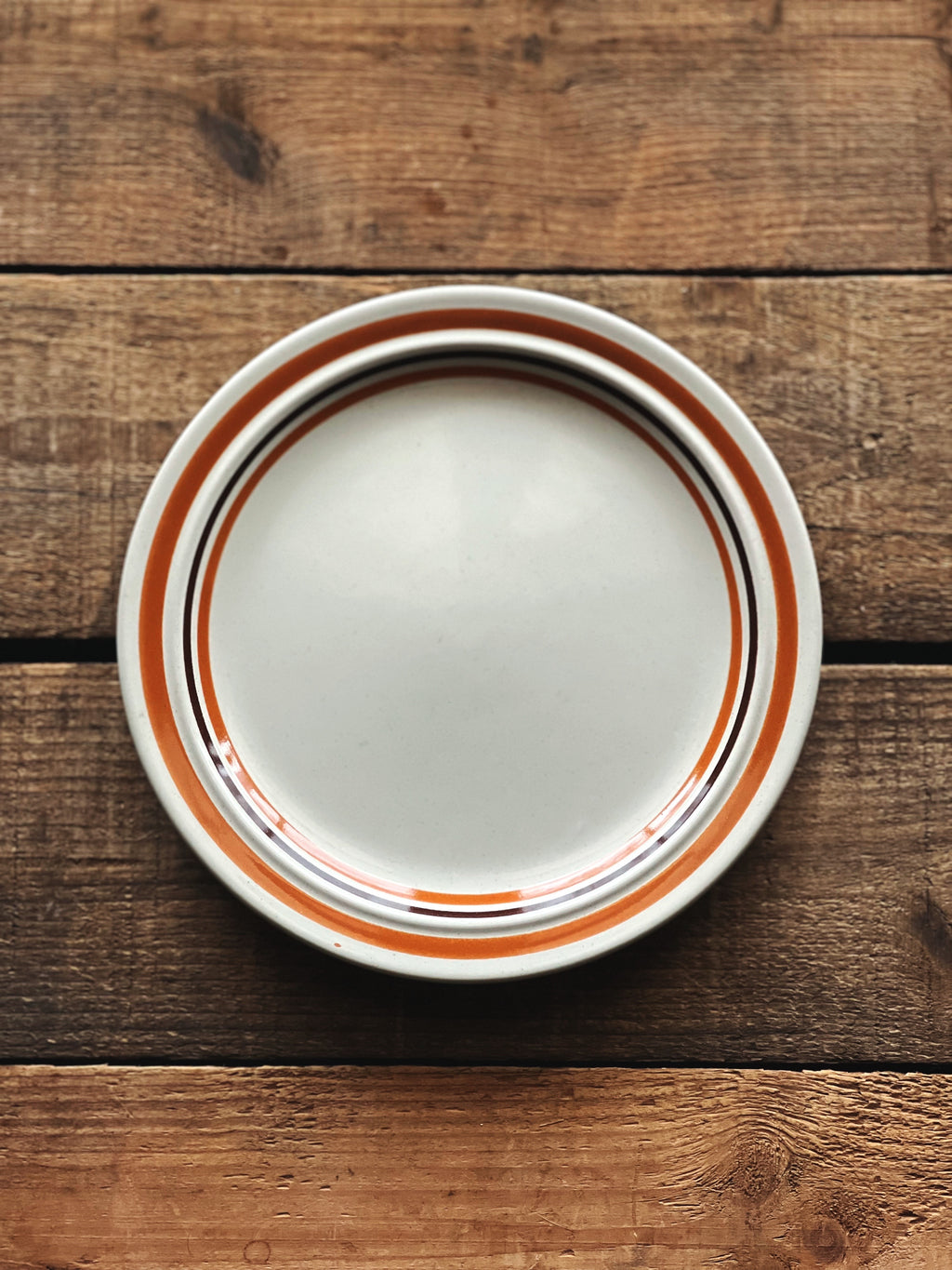 Stack of white plates with orange and black rim on a wooden surface
