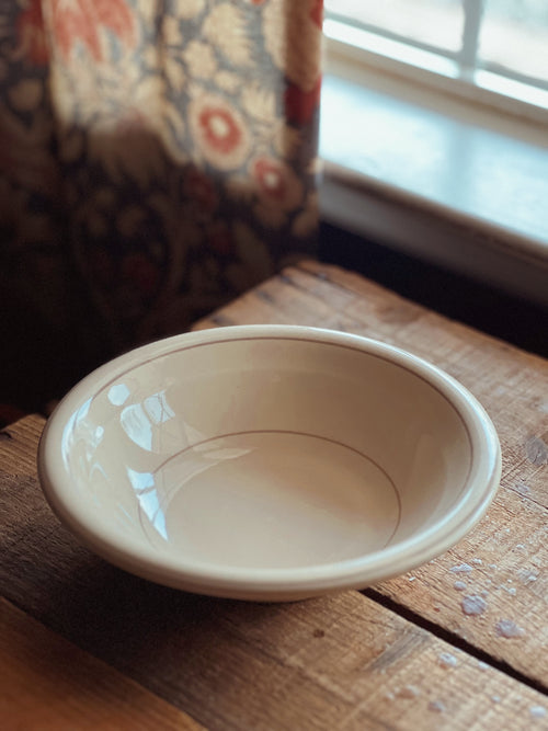 Beige ceramic bowl on a wooden surface with a floral curtain in the background