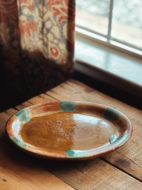 Ceramic plate with brown and green glaze on a wooden surface near a window.