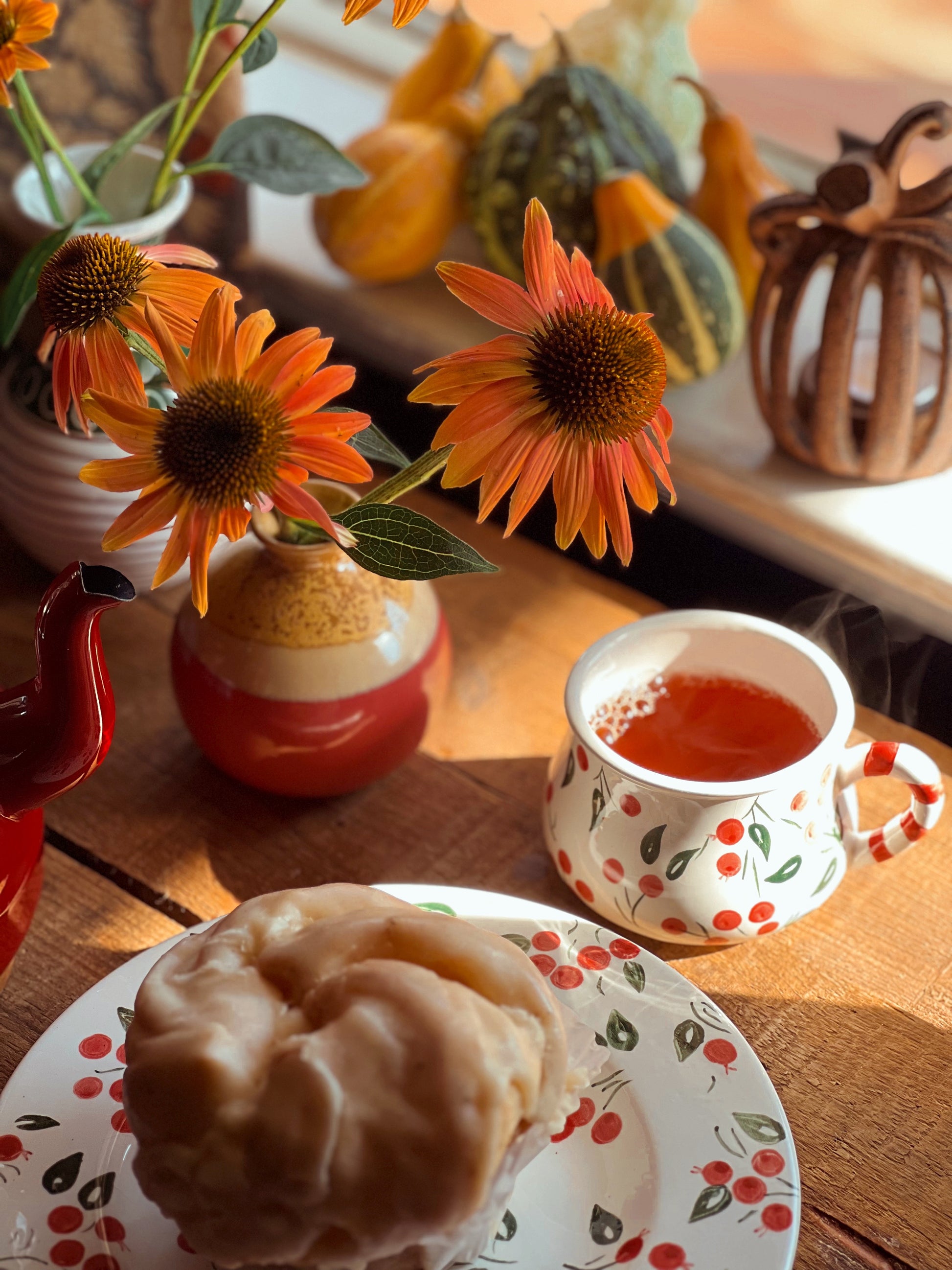 Tea cup with red liquid on a plate with a pastry, surrounded by autumn decorations.