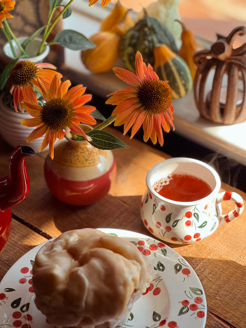 Tea cup with red liquid on a plate with a pastry, surrounded by autumn decorations.