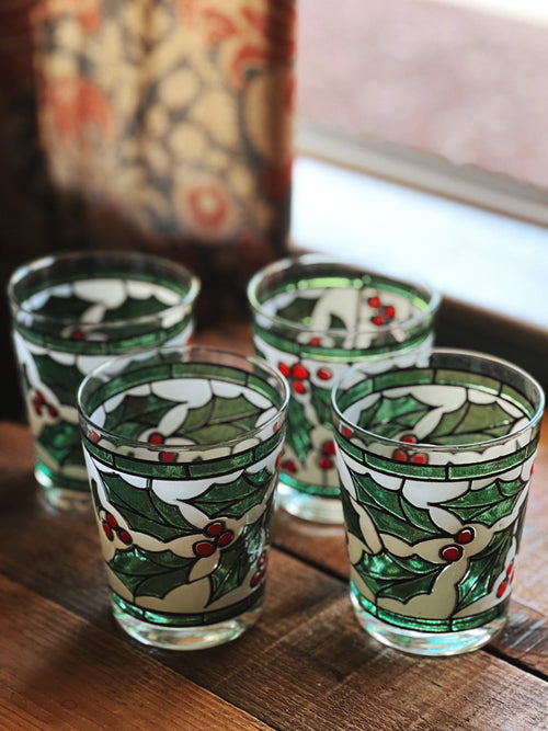 Set of four decorative shot glasses with holly design on a wooden surface.