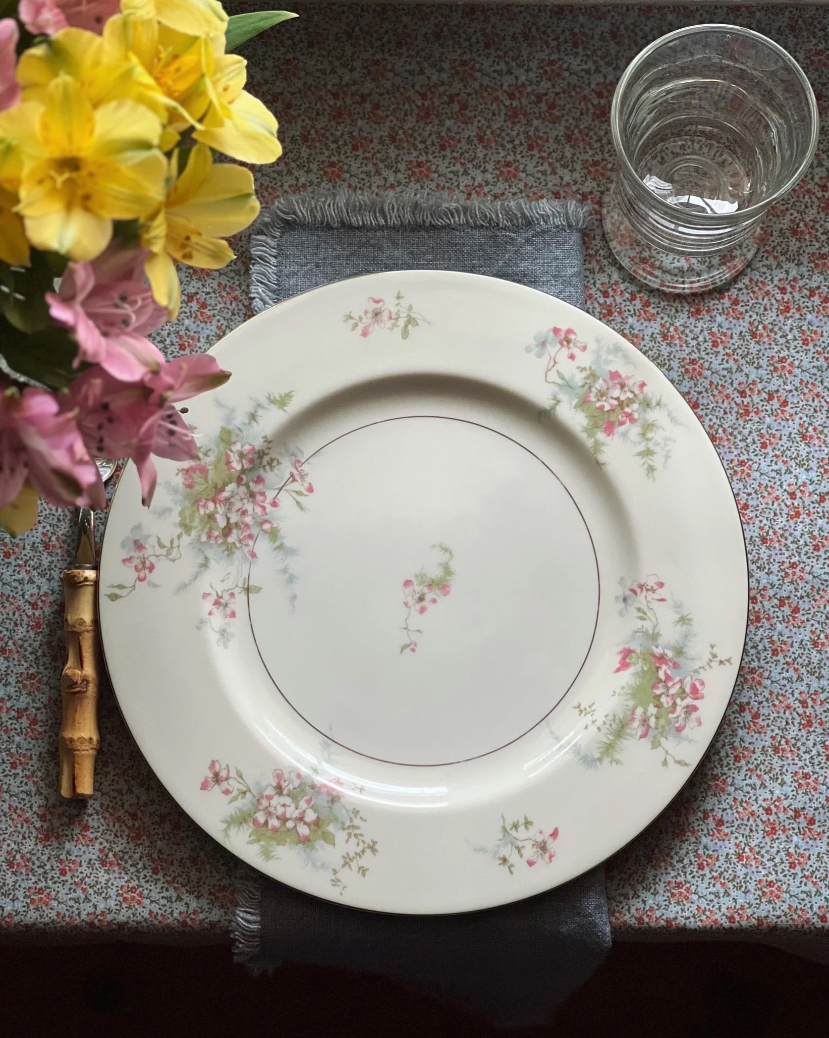 pink blue and green floral dinner plate set on a table with a blue floral tablecloth and chambray napkin