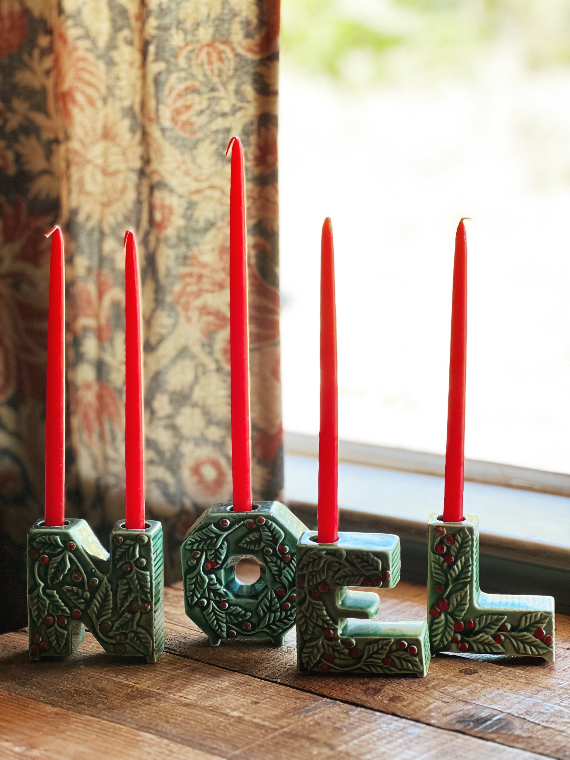 Decorative candle holders spelling 'NOEL' with red candles on a wooden surface.