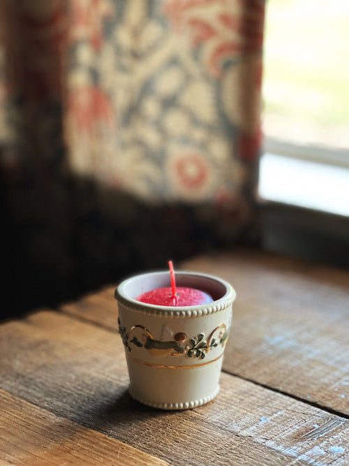 Pink candle in a decorative holder on a wooden surface with a floral curtain in the background