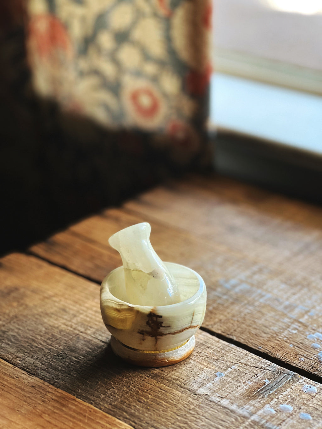 Small white marble mortar and pestle on a wooden surface with a blurred background