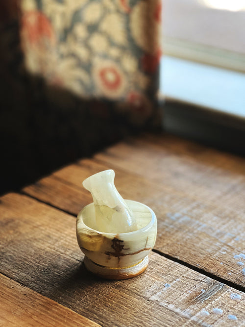 Small white marble mortar and pestle on a wooden surface with a blurred background