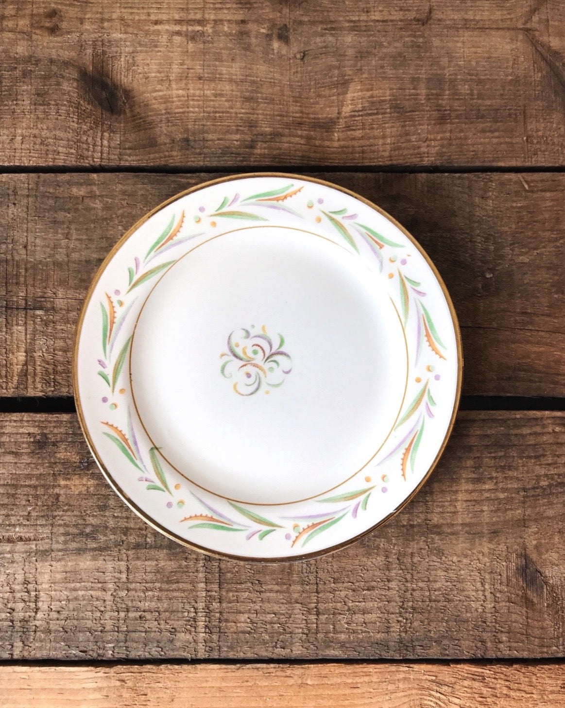 A set of four Homer Laughlin Eggshell Nautilus dessert plates with gold banded edges and floral patterns in purple, green, and yellow colors.