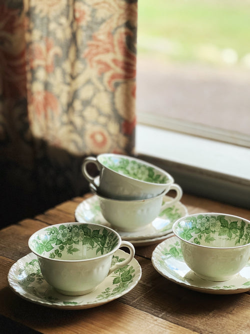 Set of white teacups with green floral patterns on a wooden table.