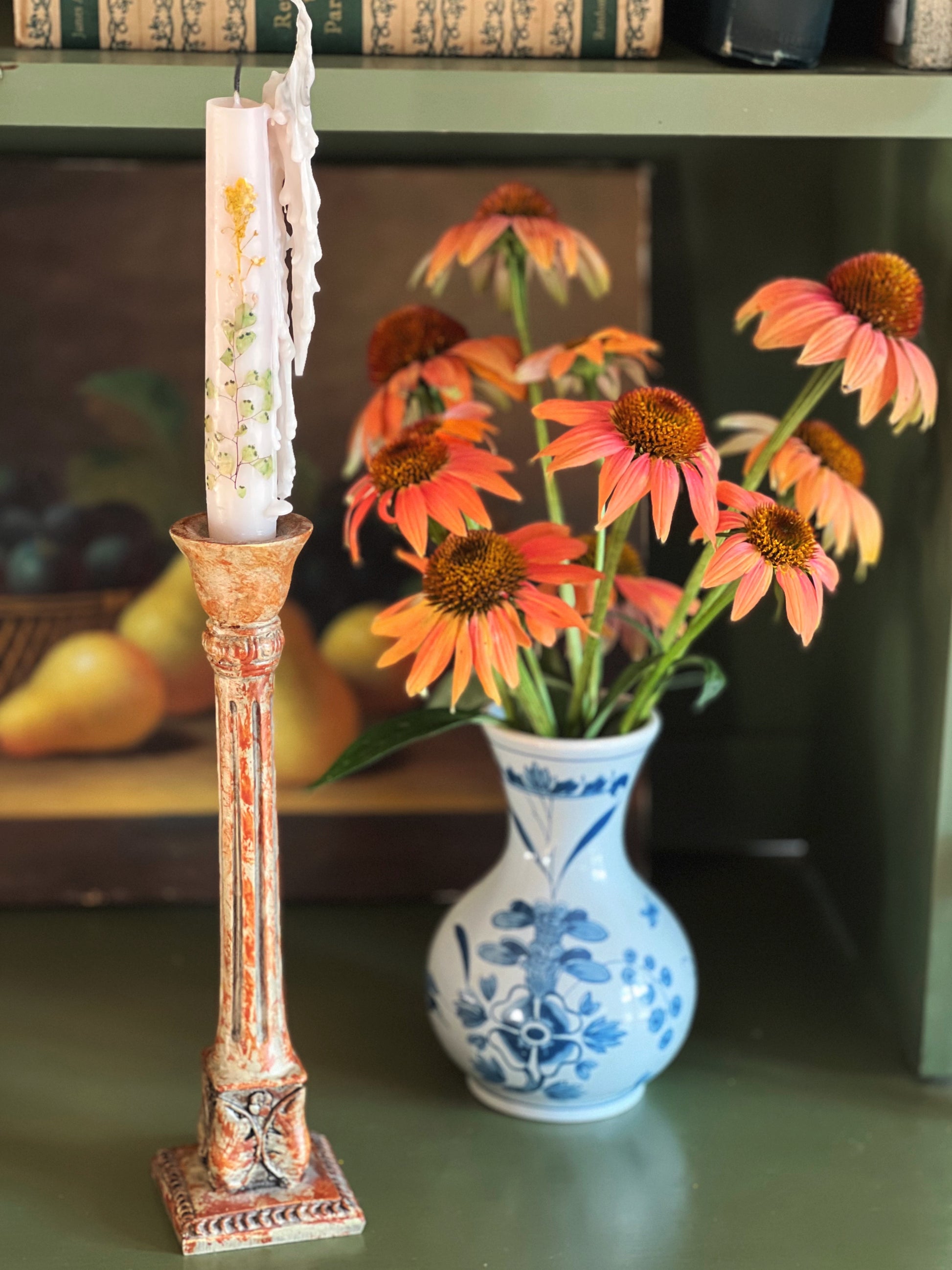 Decorative candlestick with a candle, vase with flowers, and books in the background.