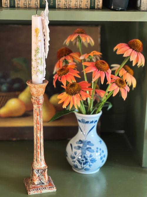 Decorative candlestick with a candle, vase with flowers, and books in the background.
