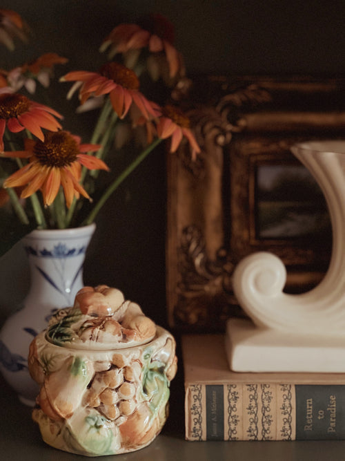 Decorative ceramic pot with lid on a surface with books and flowers in the background
